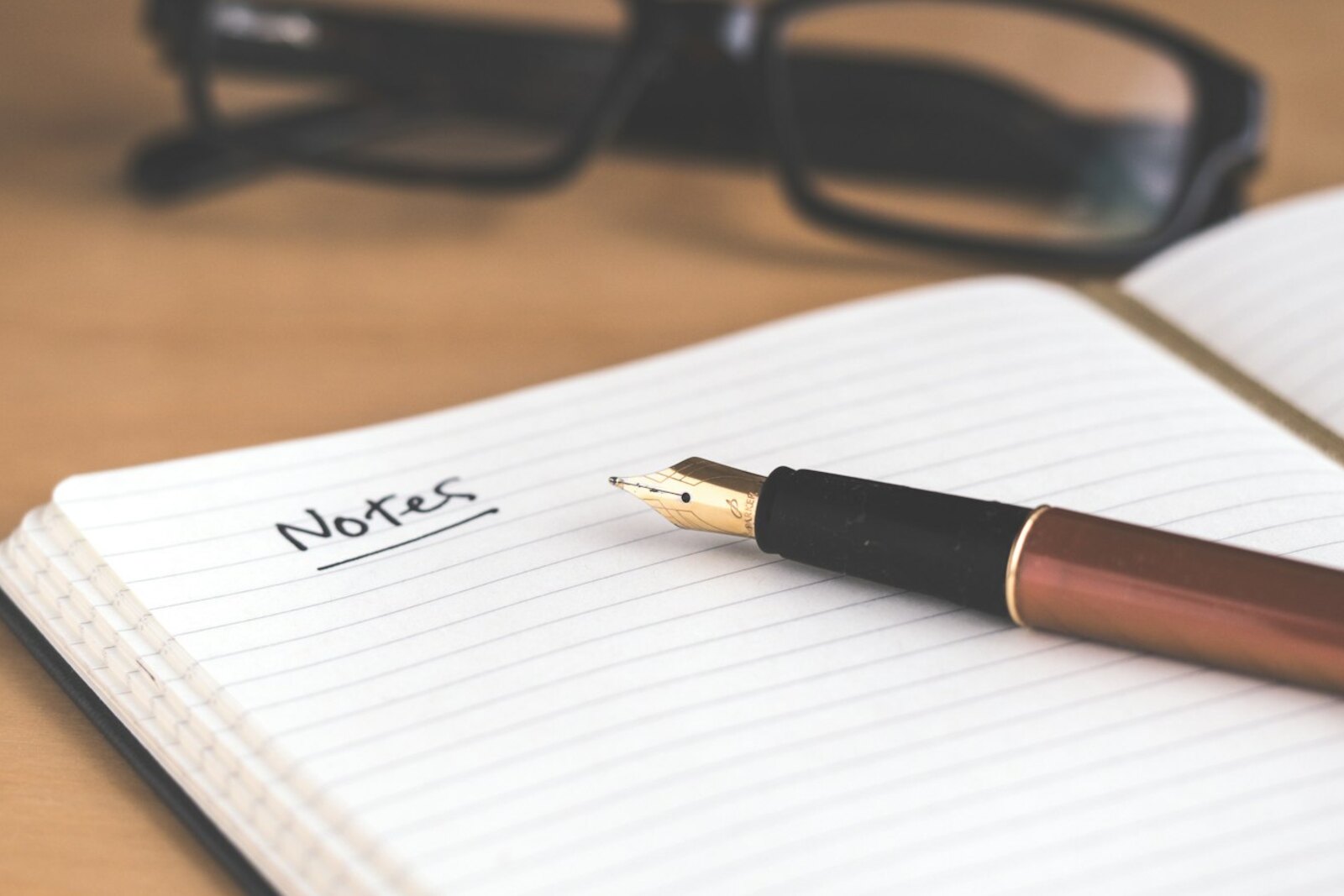 A black pen lying on a blank open notebook in soft window light